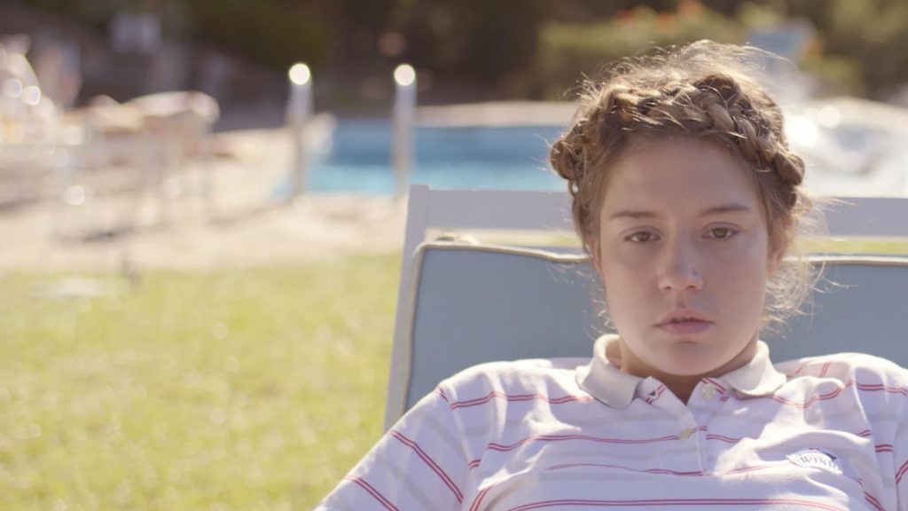 Magalie, jeune femme au regard vide, est assise sur un transat au bord d’une piscine dans L’accident de piano de Quentin Dupieux.
