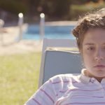 Magalie, jeune femme au regard vide, est assise sur un transat au bord d’une piscine dans L’accident de piano de Quentin Dupieux.